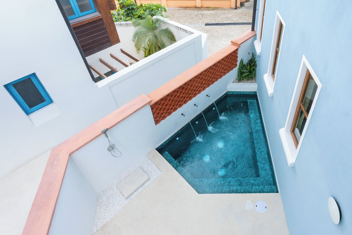 Un edificio moderno con piscina, una zona de estar al aire libre techada y un pequeño jardín.