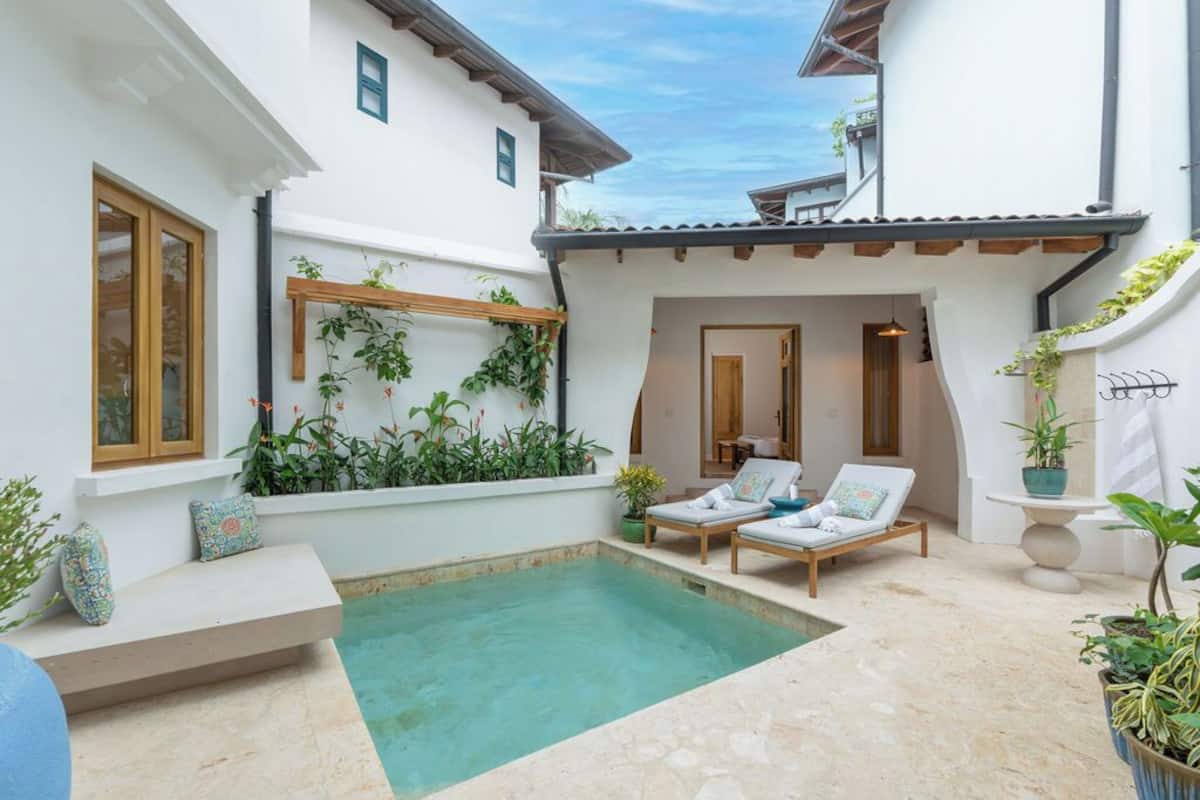 Zona junto a la piscina con una pequeña alberca, sillas de descanso y plantas en macetas.