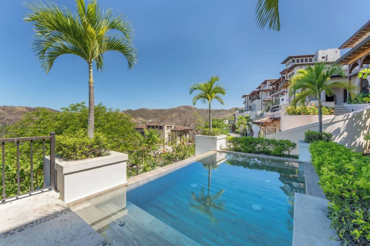 Una piscina rodeada de palmeras y una ladera en el fondo.