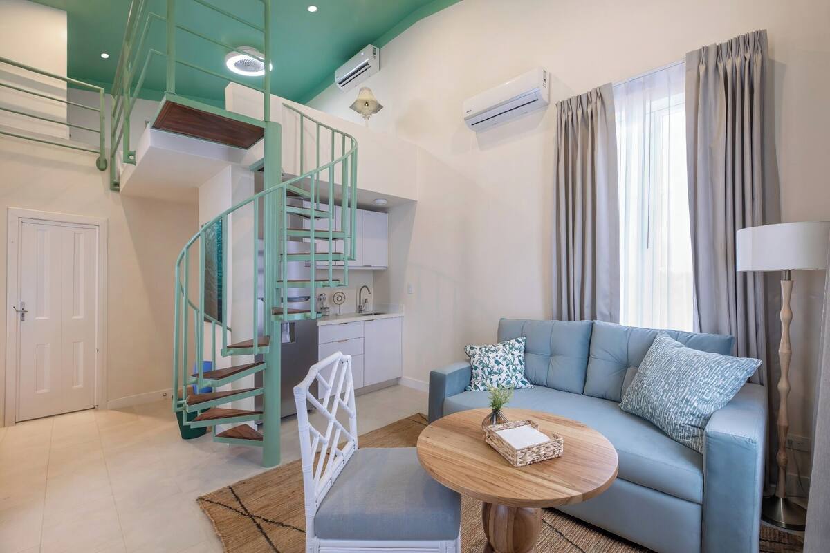 Una sala moderna con un sofá azul, una mesa de centro redonda de madera y una escalera espiral verde.