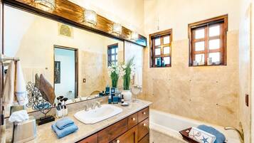 A bathroom with a large mirror, wooden vanity, and a bathtub.