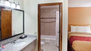 A hotel bathroom with a sink, mirror, shower, and a bed with pillows. - Econo Lodge Phillipsburg (Phillipsburg)