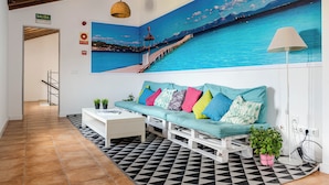 A lobby with a teal sofa, a white coffee table, a black and white patterned rug, and a large mural of a coastal scene. - Urban Hostel Palma Albergue Juvenil (Palma de Mallorca)