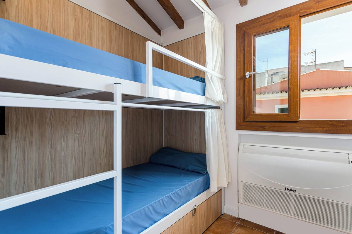 A bunk bed with a blue mattress, wooden paneling, and a window with a wooden frame.