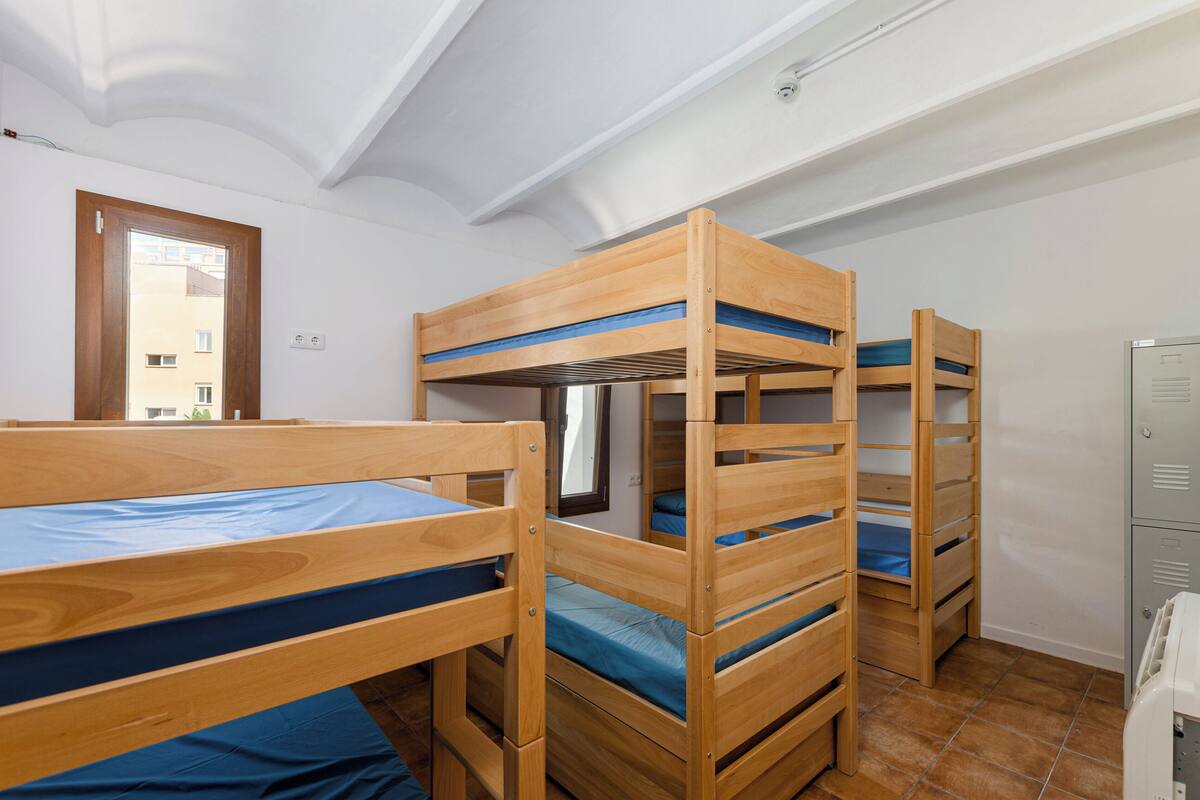 A dormitory room with bunk beds, a window, and a door.