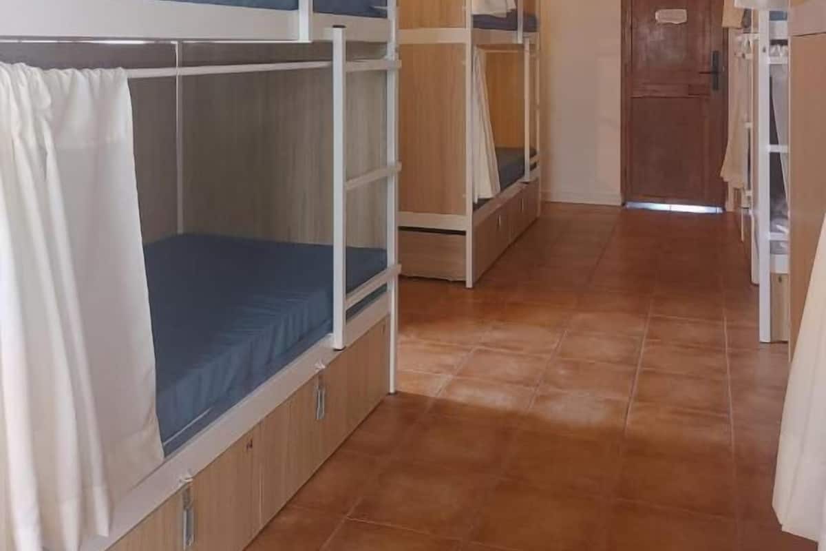 A dormitory room with bunk beds, wooden beams, and a tiled floor.