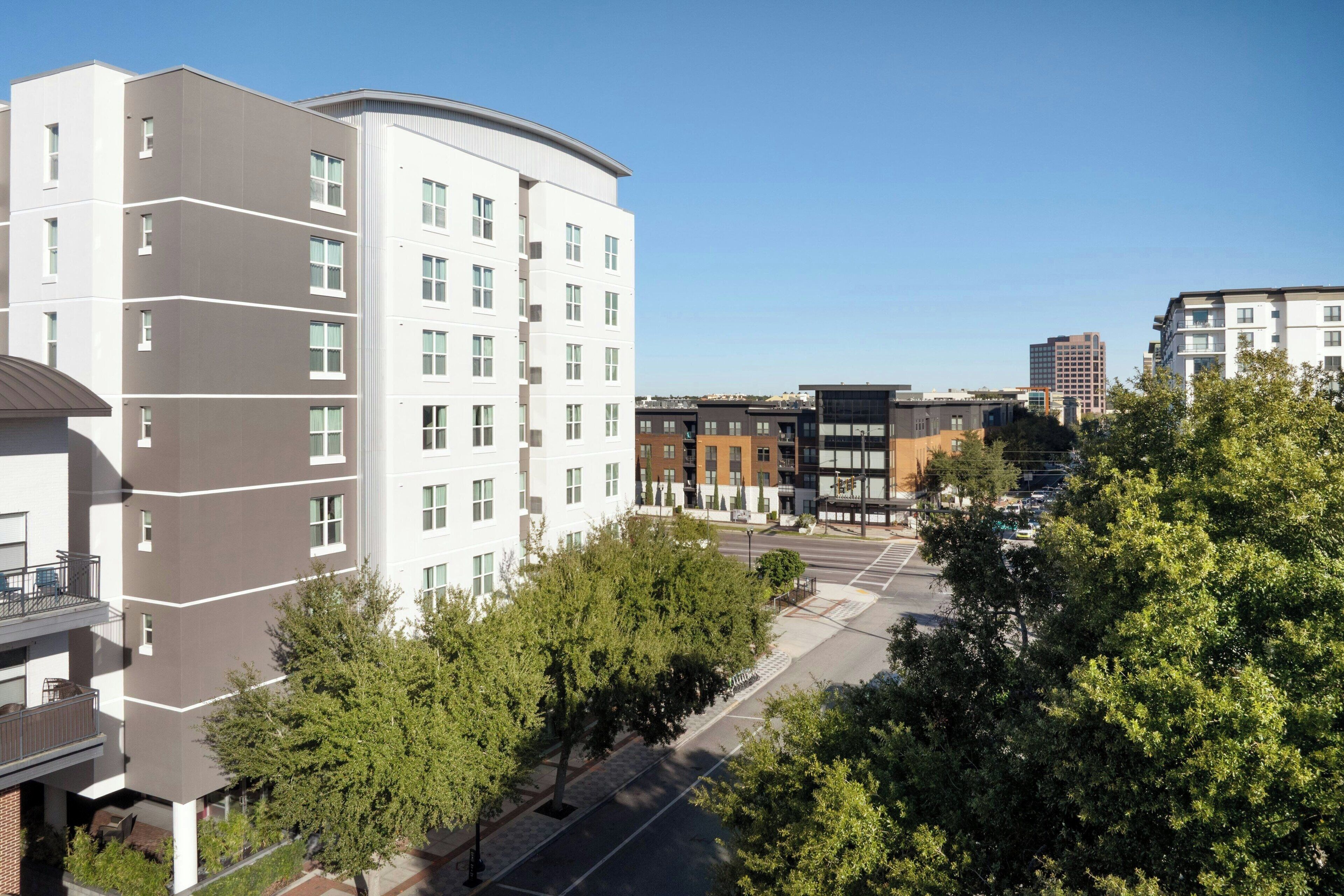 A multi-story residential building with balconies, a parking area, and a clear sky.