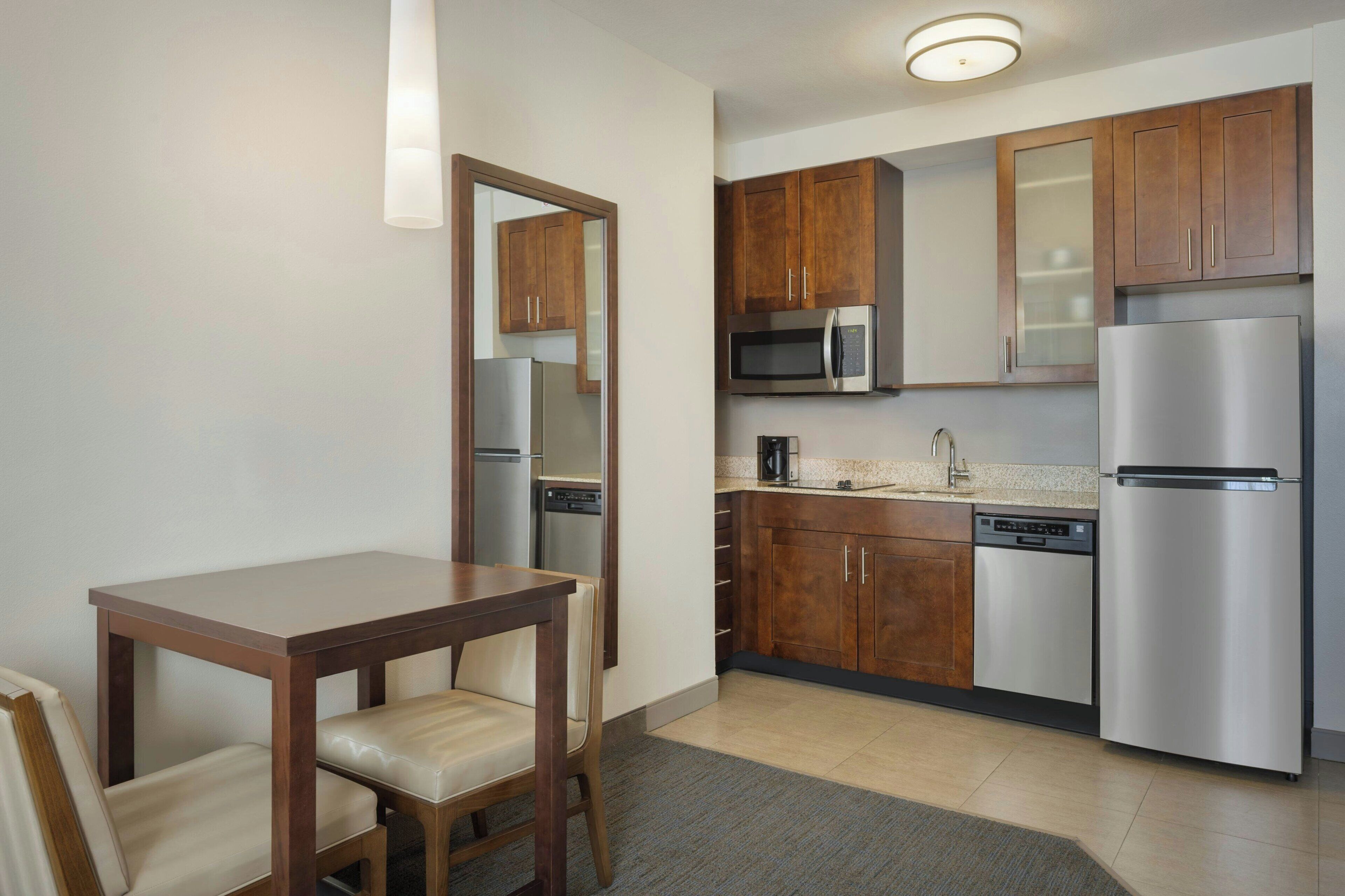 A compact kitchen with wooden cabinets, stainless steel appliances, and a small dining table with chairs.