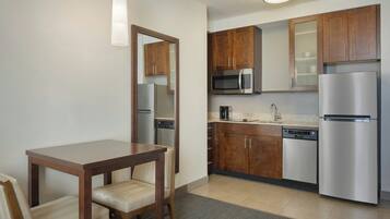 A compact kitchen with wooden cabinets, stainless steel appliances, and a small dining table with chairs.