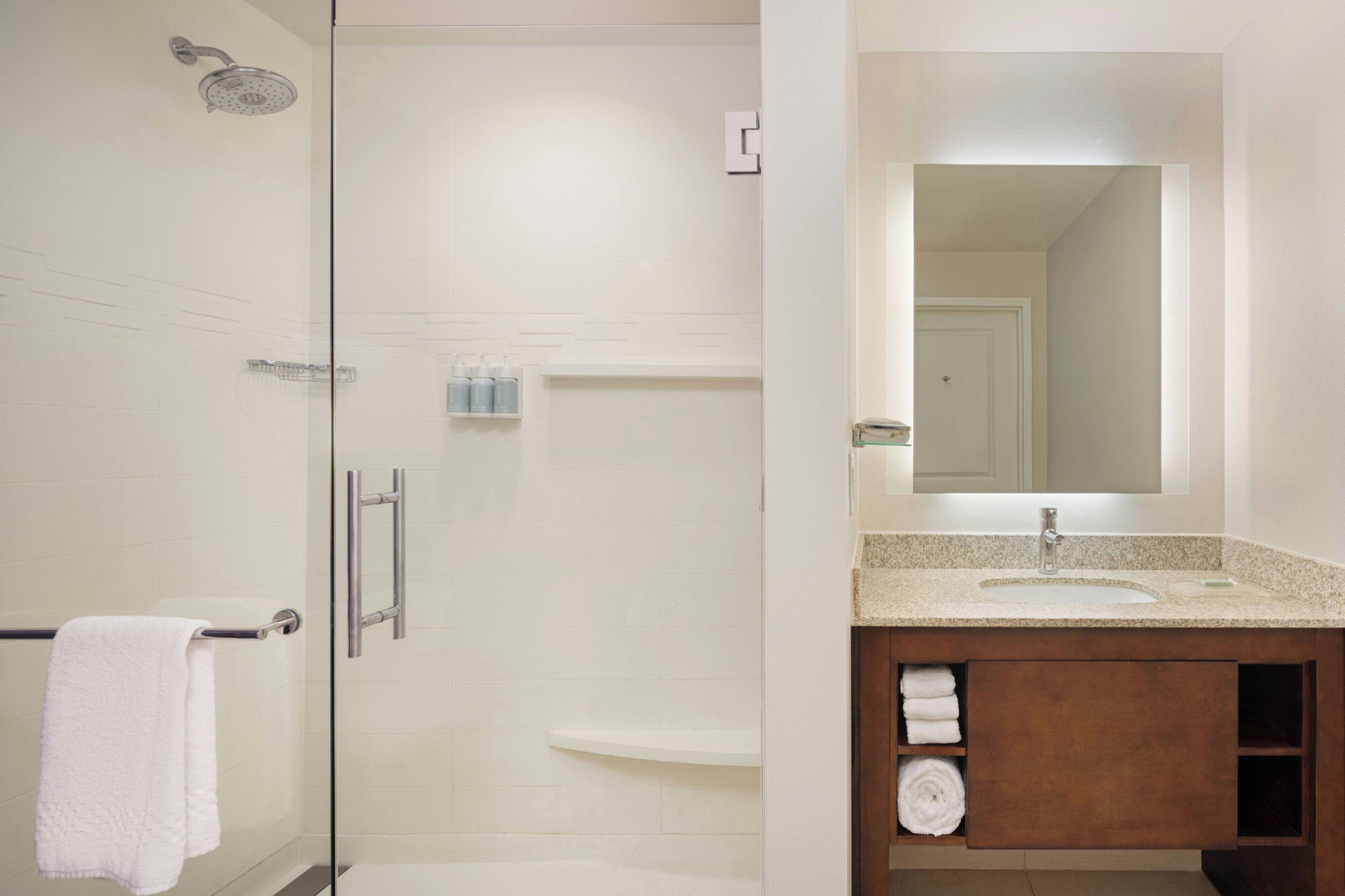 A modern bathroom with a glass shower enclosure, a white sink with a large mirror, and a wooden vanity with towels.
