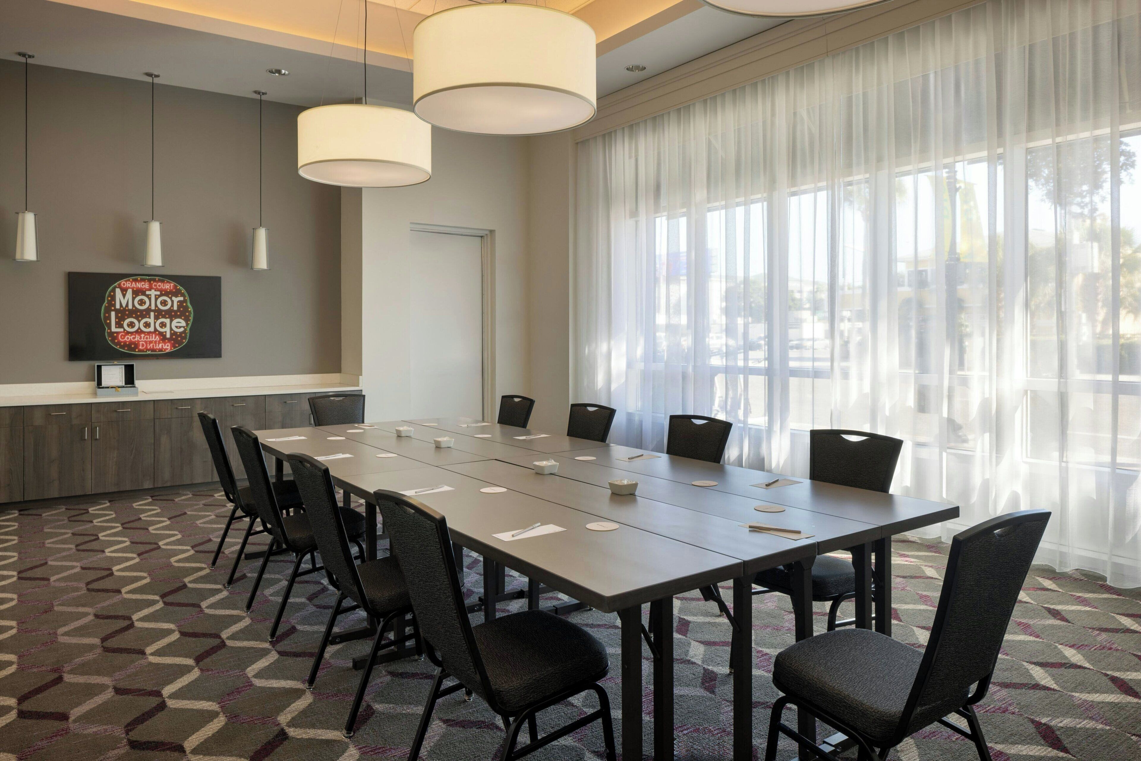 A conference room with a long table, chairs, and a large window with sheer curtains.