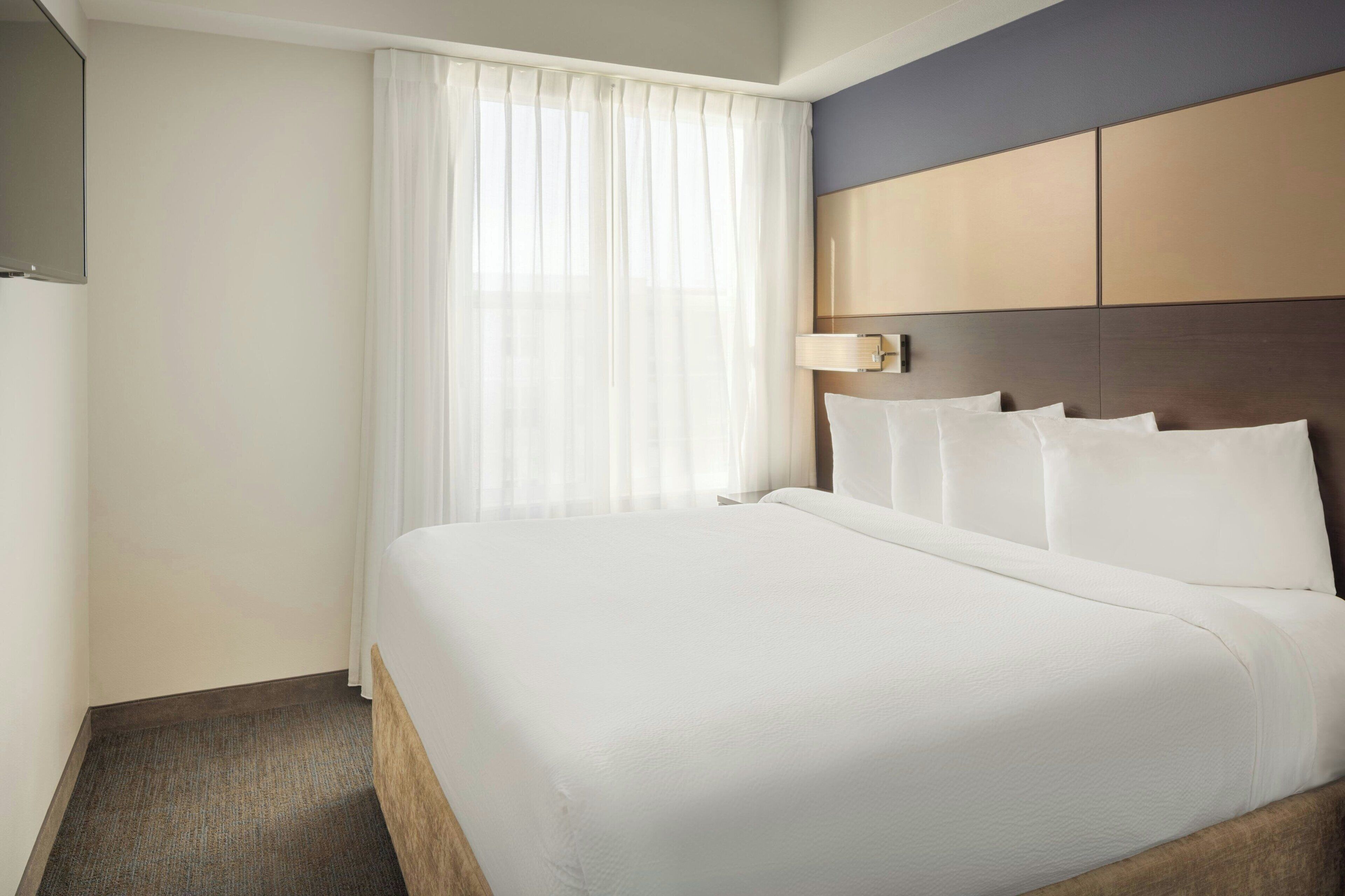 A hotel room with a large bed, a headboard, a bedside table, and a window with curtains.