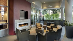 A modern outdoor living area with a fireplace, comfortable seating, and large windows offering views of greenery. - Residence Inn by Marriott Orlando Downtown (Orlando)