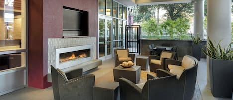 Un espacio exterior moderno con chimenea, asientos cómodos y grandes ventanales con vistas a la vegetación.