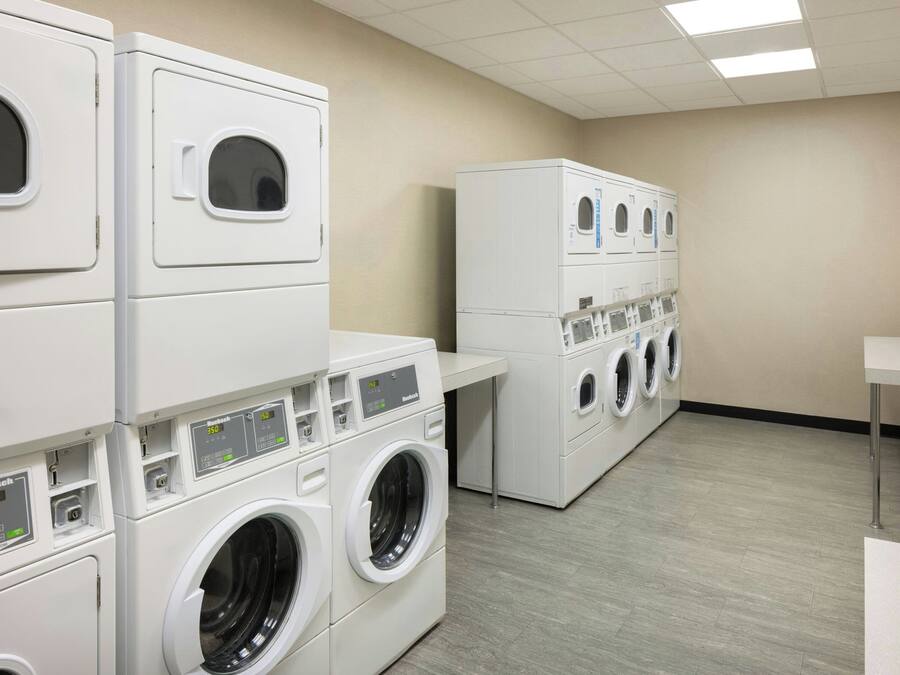 A laundry facility with stacked washing machines and dryers, a white tiled floor, and a plain wall.