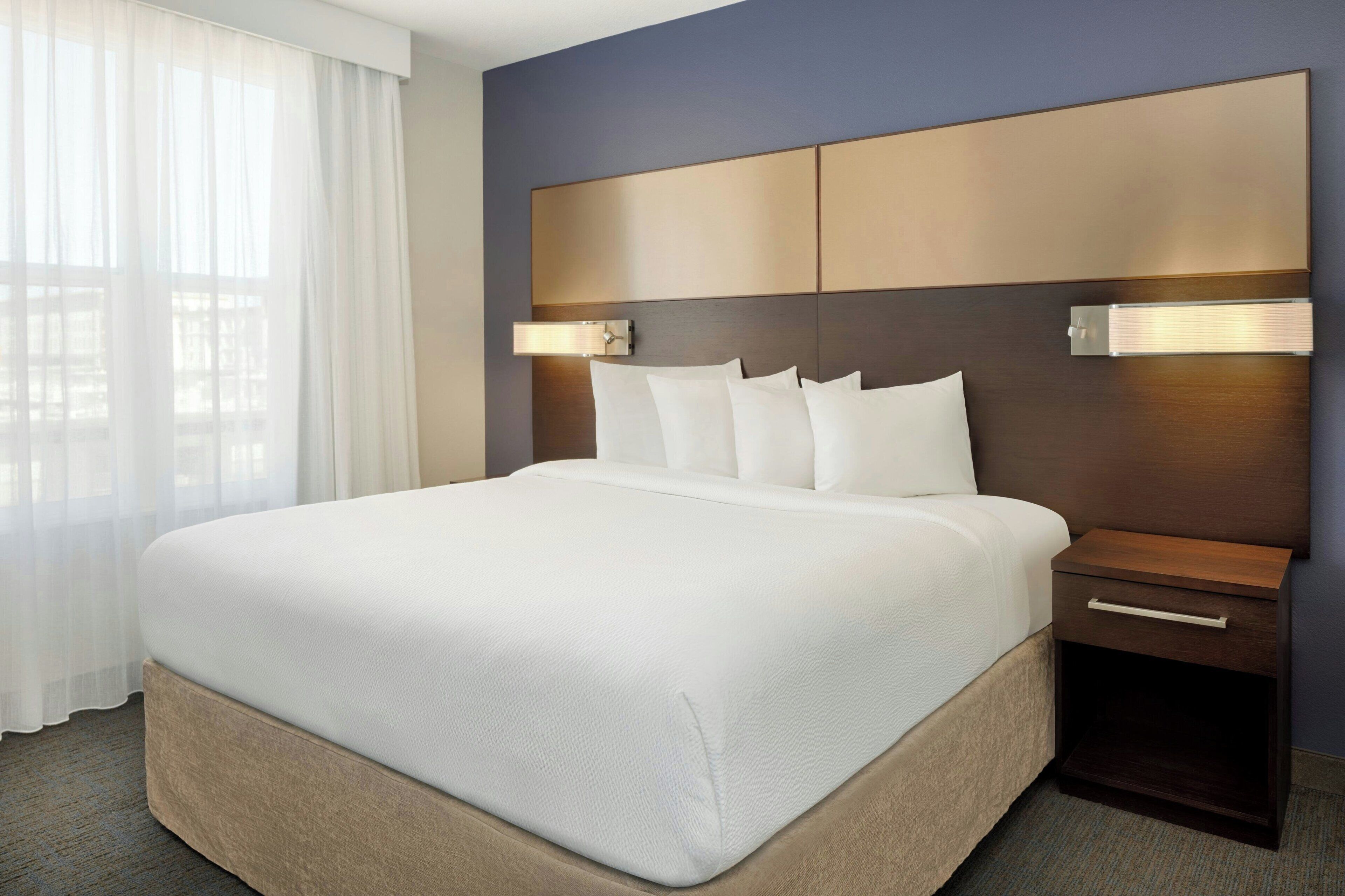 A hotel room with a large bed, a wooden headboard, bedside lamps, and a nightstand.