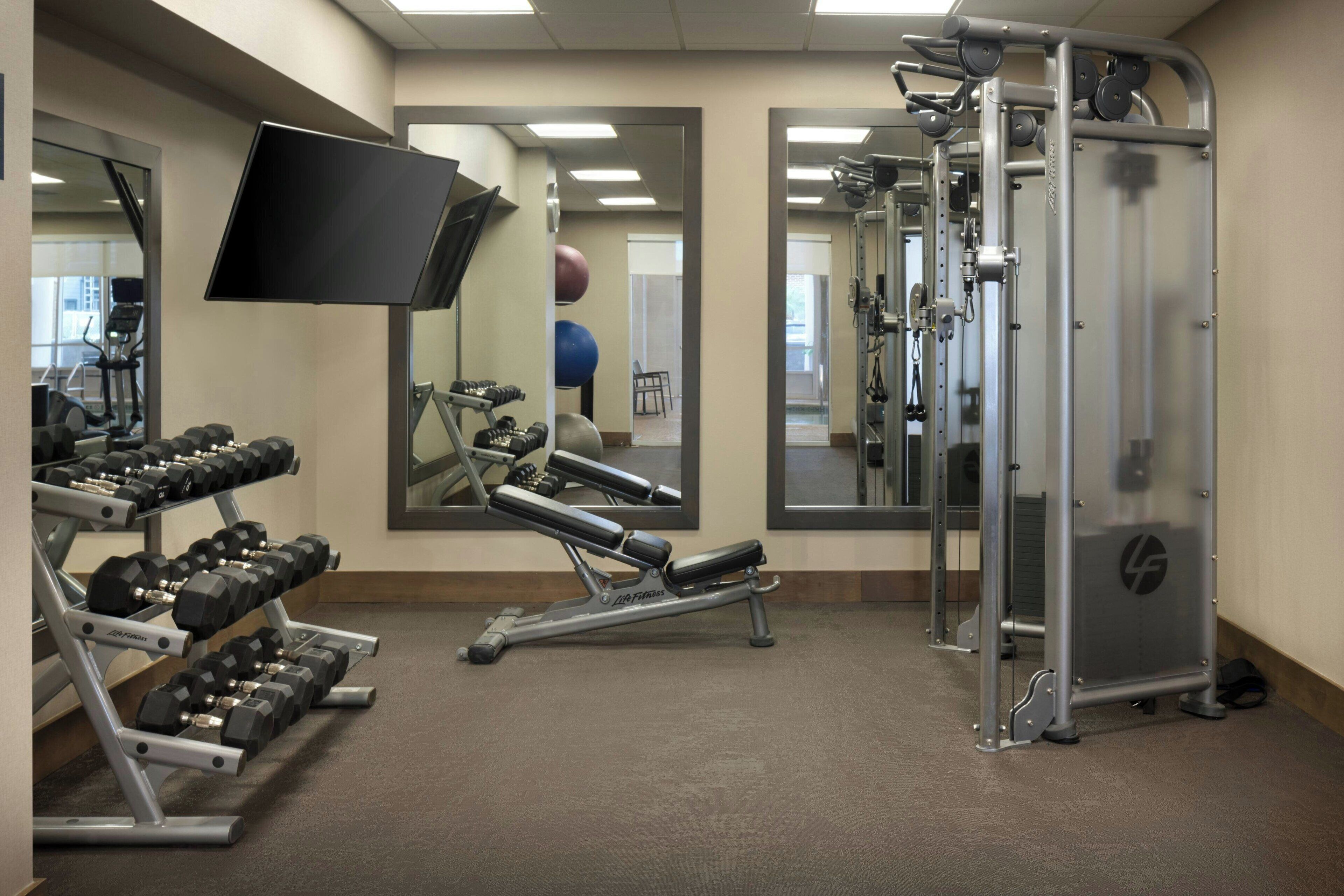 Ein Fitnessraum mit Trainingsgeräten, einem Fernseher und Spiegeln.