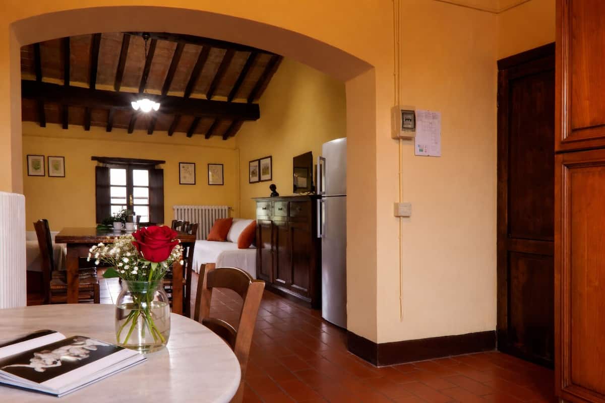 Un comedor con una mesa, sillas, un jarrón con flores, un libro y una cocina al fondo.