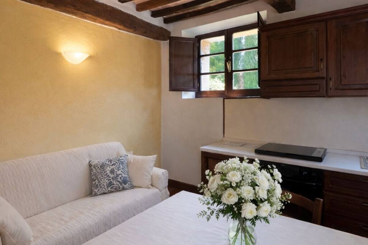 Habitación con sofá, una mesa con un florero, vigas de madera en el techo y ventana con vistas a la vegetación.