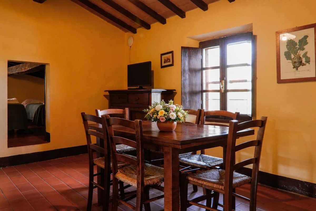 Un comedor con una mesa de madera, sillas, un jarrón de flores, un reloj y una puerta.