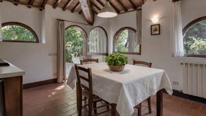 A dining area with a table, chairs, a potted plant, and arched windows with curtains.