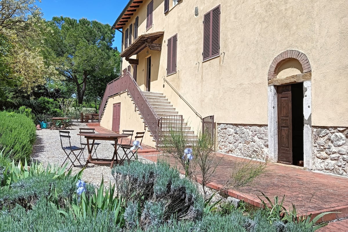 Un edificio con fachada de piedra, una escalera de madera y un jardín con muebles de exterior.