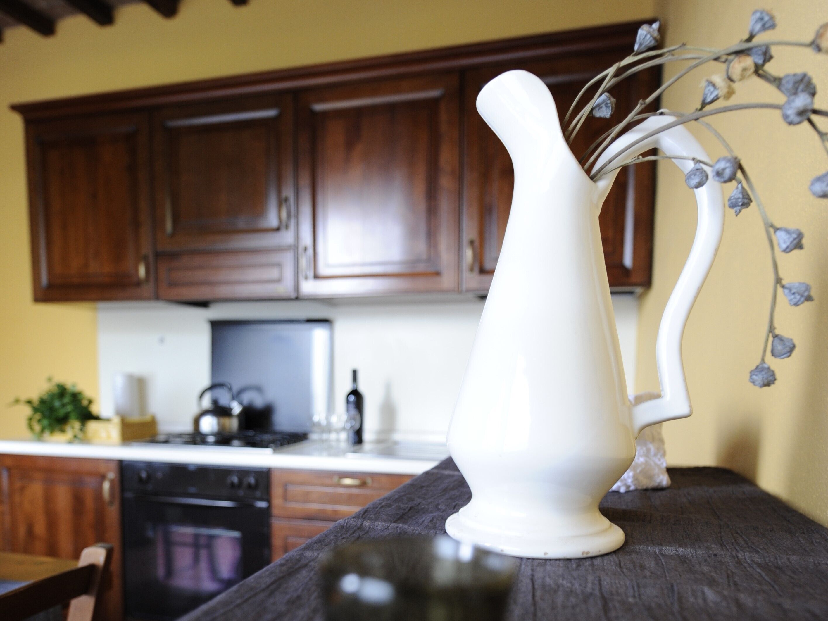 A kitchen with wooden cabinets, a white pitcher on a table, and a decorative wall piece.
