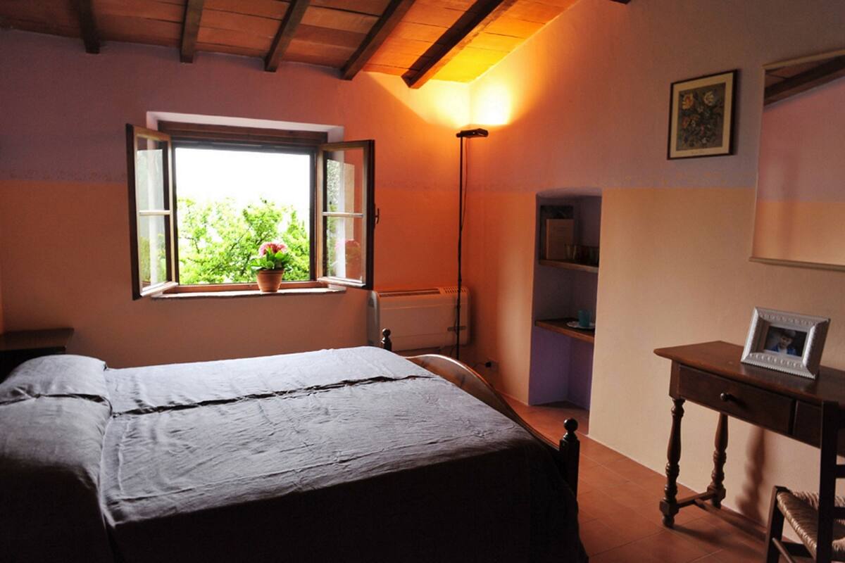 Un dormitorio con cama, ventana con vistas, mesita de noche y lámpara.
