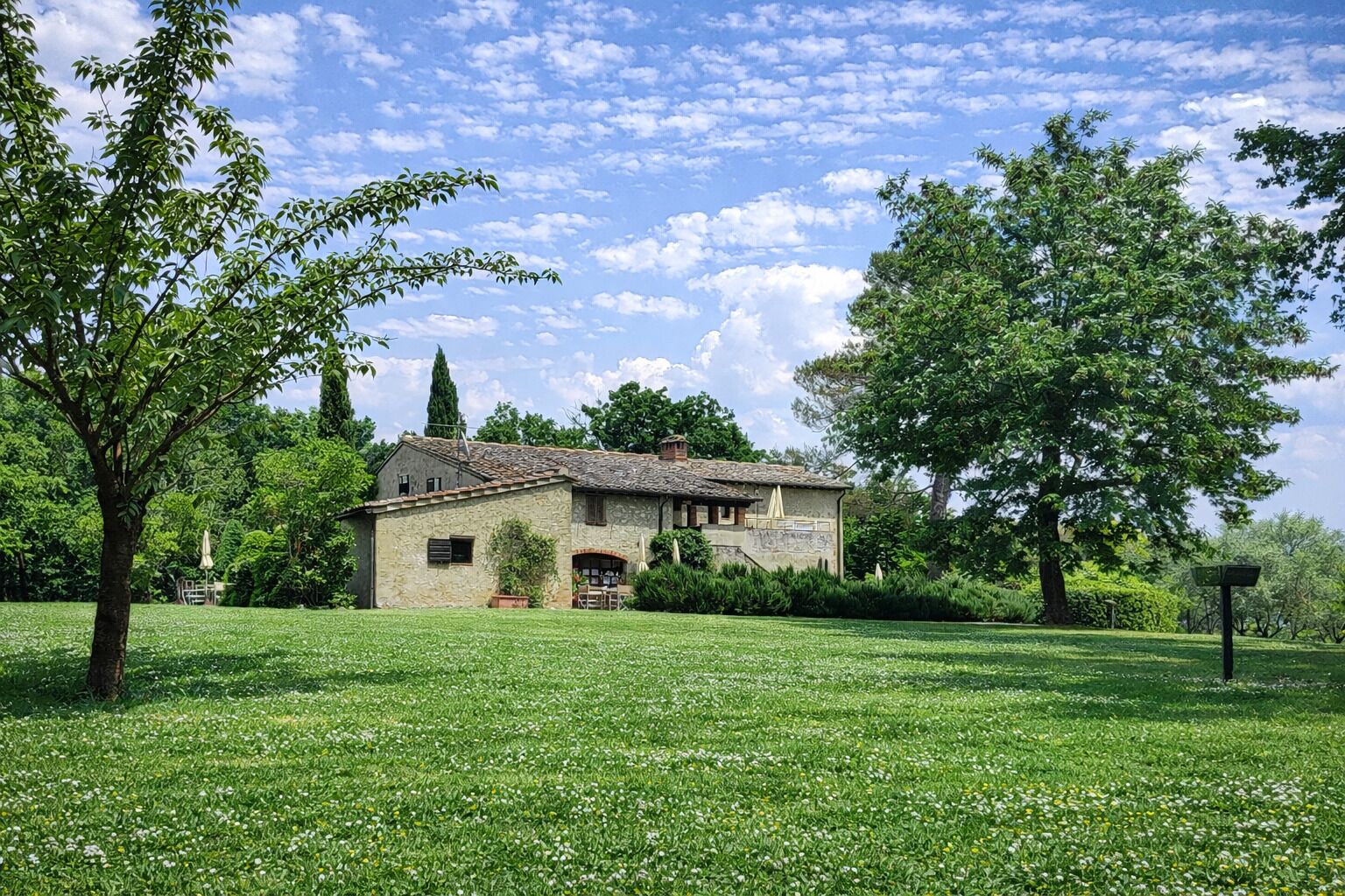 A stone house with a tiled roof, surrounded by a lush green lawn and trees.