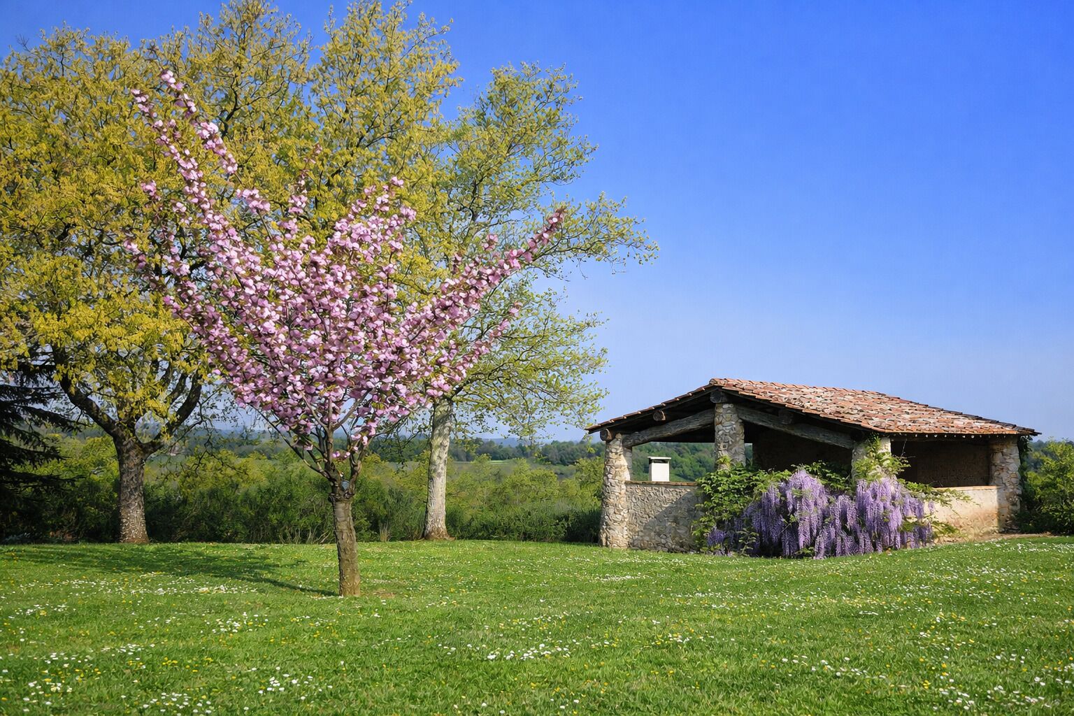 A rustic stone building with a tiled roof, surrounded by a lush green field and blooming trees.