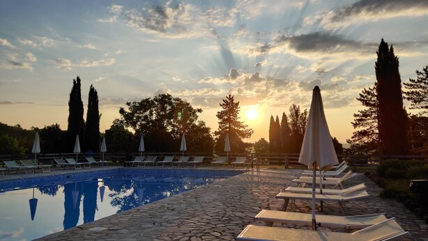 A poolside area with lounge chairs and umbrellas, surrounded by stone tiles and trees.