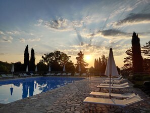 A poolside area with lounge chairs and umbrellas, surrounded by stone tiles and trees. - Agriturismo Nerbona (Colle di Val d'Elsa)