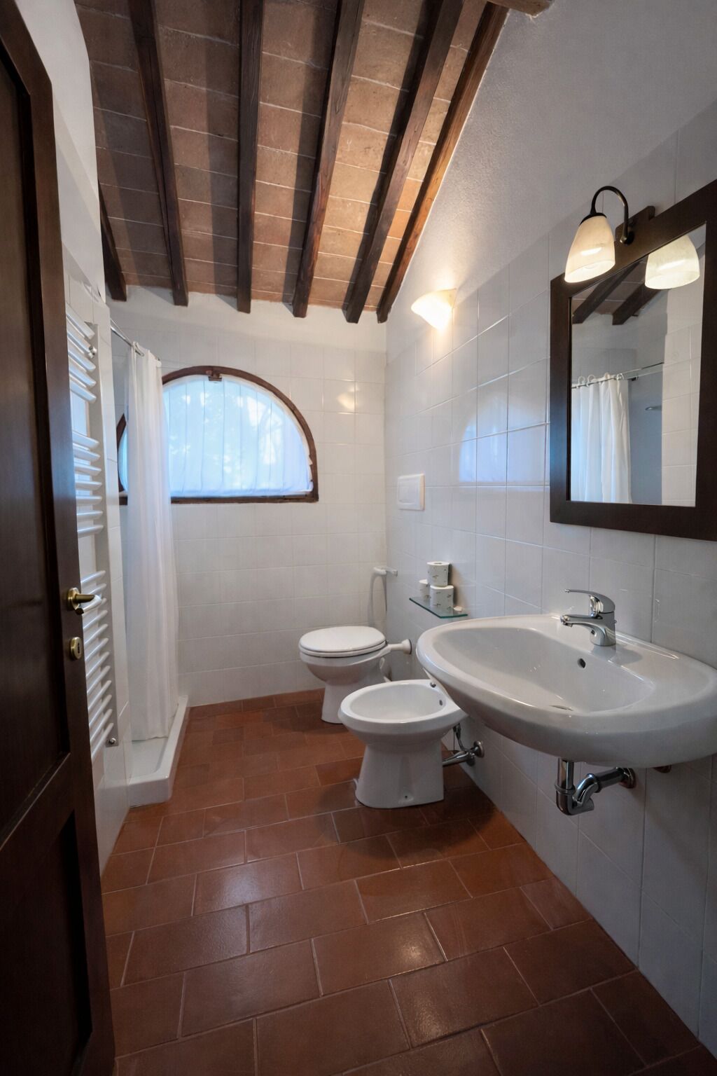 A bathroom with a large sink, two toilets, a mirror, and a window.