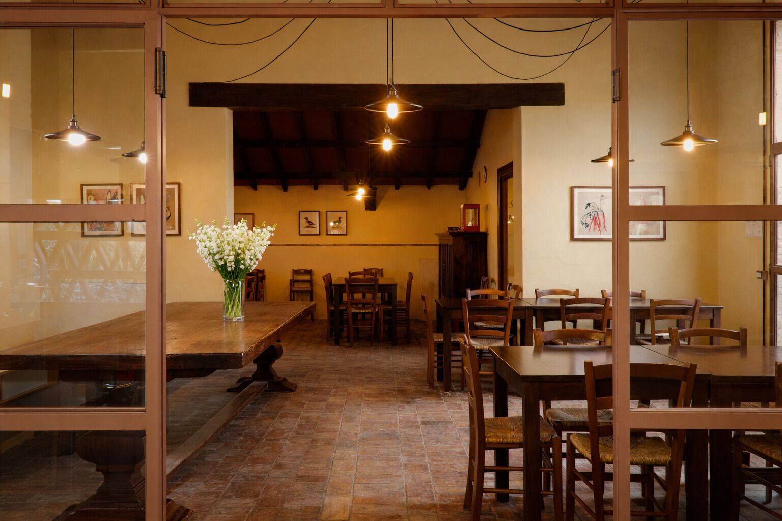 Un restaurante con una larga mesa de madera, múltiples sillas, lámparas colgantes y cuadros en las paredes.