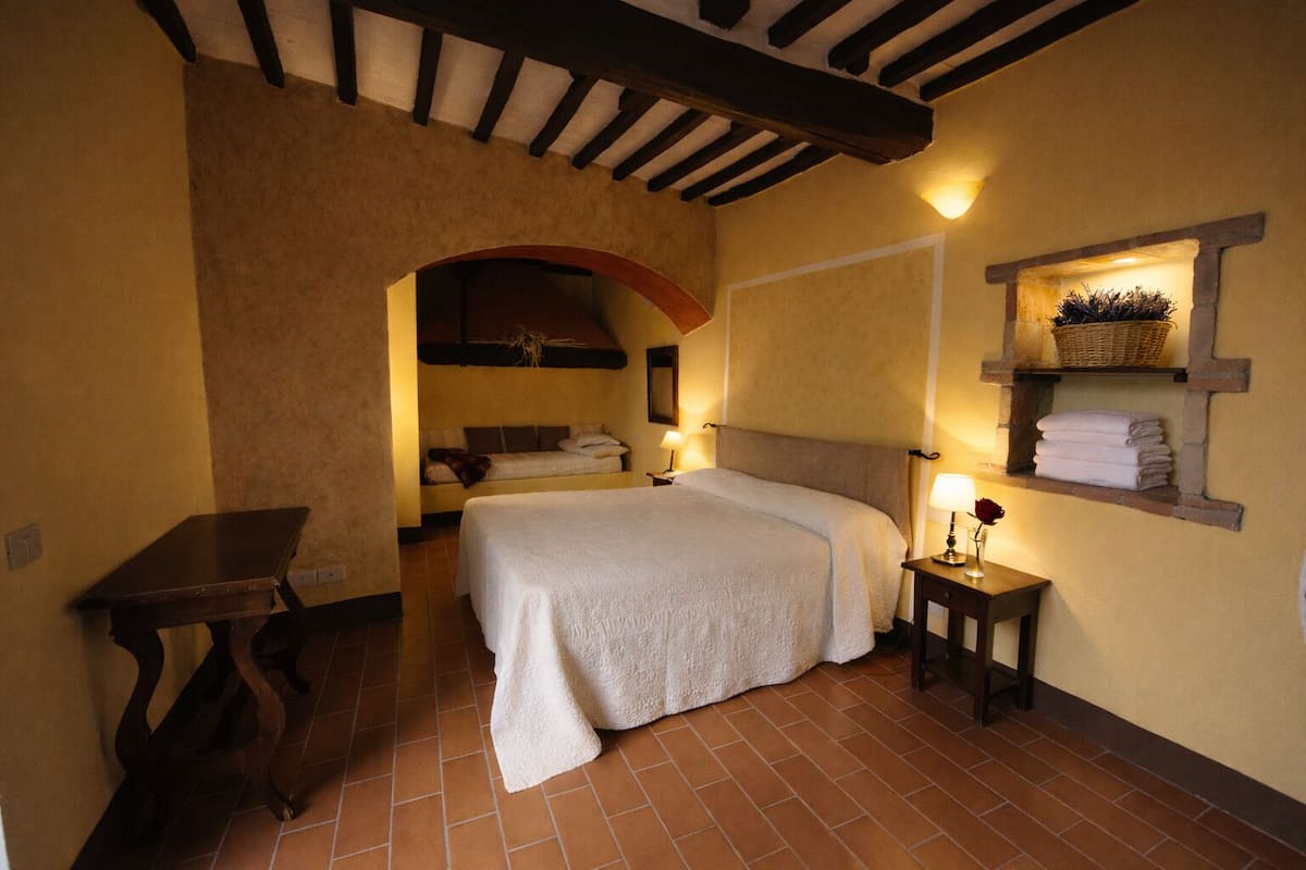 Un dormitorio con cama, escritorio, estante con toallas y una lámpara de pared.