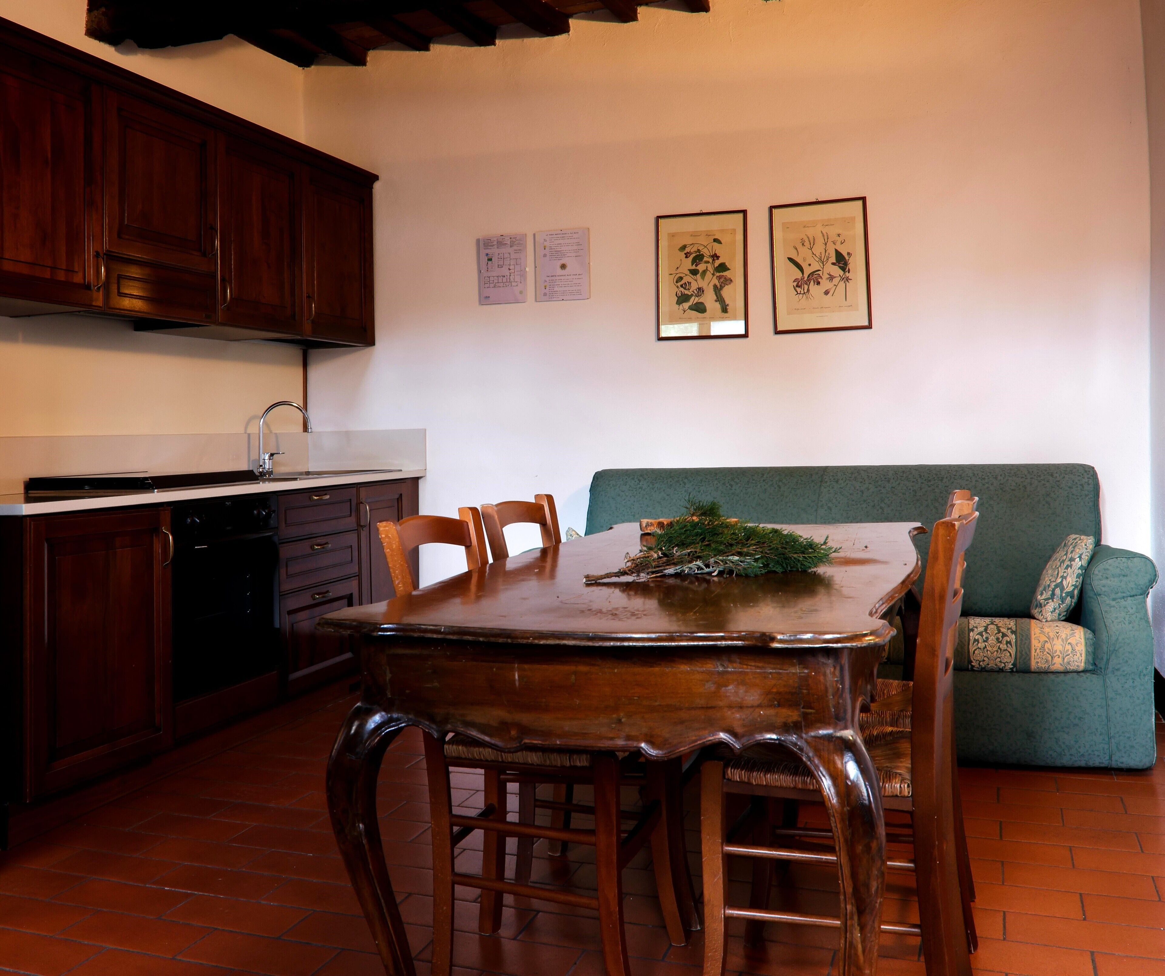 Una cucina con mobili in legno, un tavolo da pranzo con sedie, un divano verde e due stampe botaniche incorniciate appese al muro.