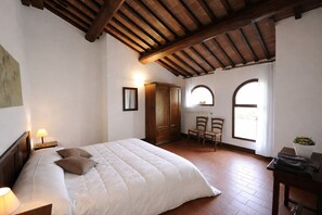 A bedroom with a large bed, wooden wardrobe, two chairs, and a desk with a plant. - Agriturismo Nerbona (Colle di Val d'Elsa)