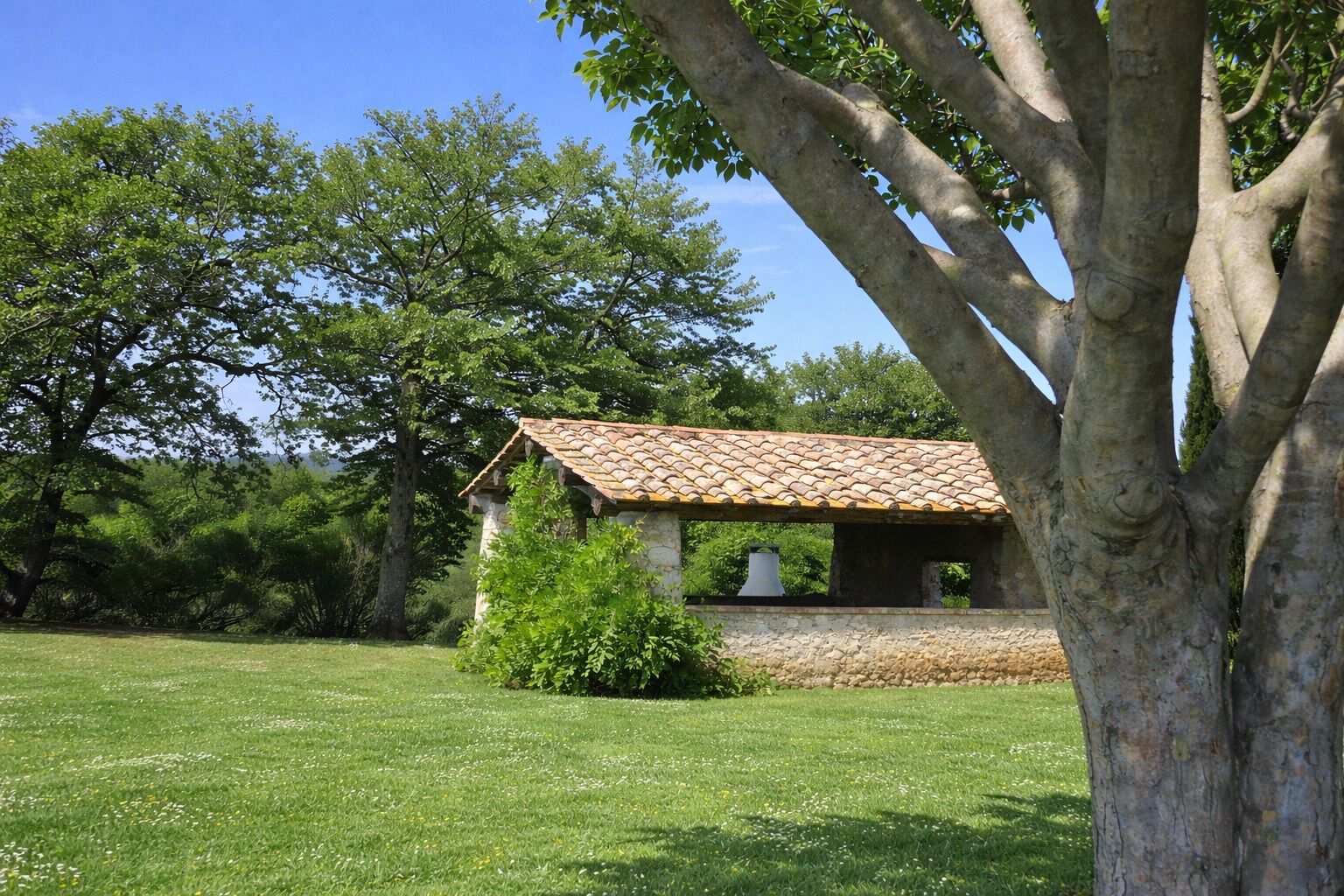 A stone building with a tiled roof, surrounded by a grassy field and trees.