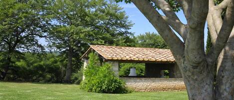 A stone building with a tiled roof, surrounded by a grassy field and trees.