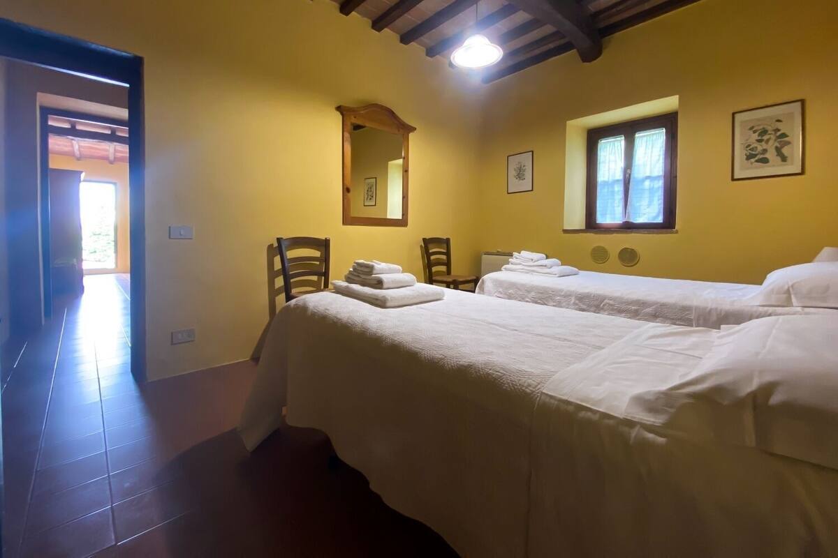 Habitación con dos camas, un espejo, una ventana y una puerta que da a un espacio luminoso.