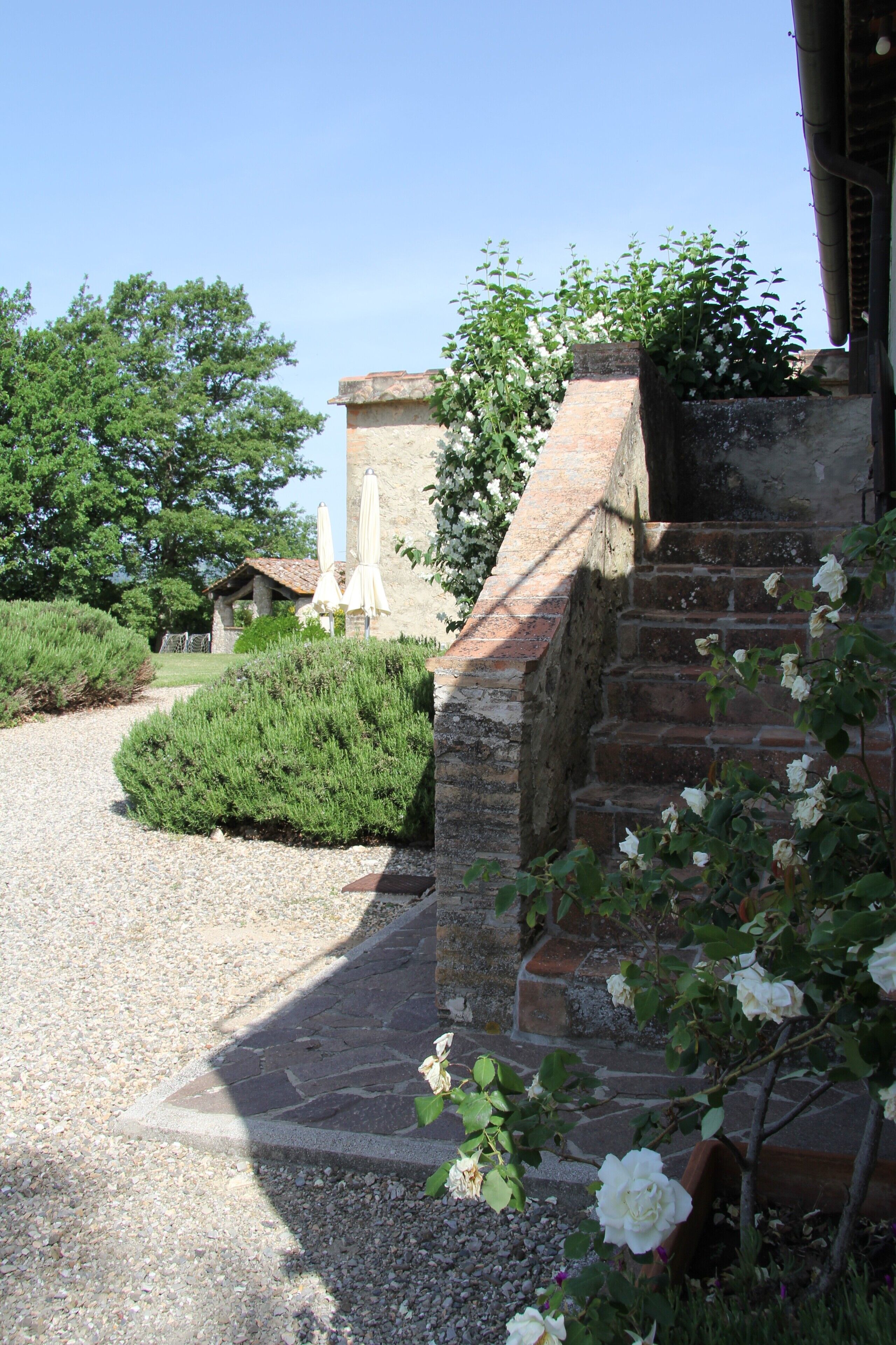 Una scala in pietra conduce a un edificio con tetto in tegole, circondato da vialetti ghiaiosi e vegetazione.