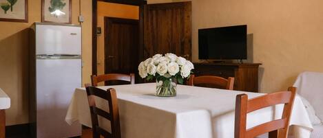 A dining area with a table set for four, a white refrigerator, a wooden cabinet, and a flat-screen TV.