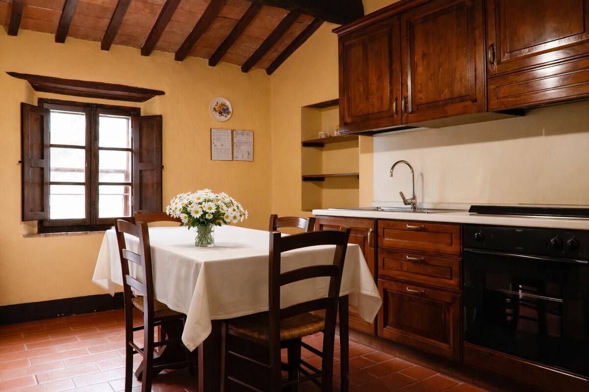 Una cocina con armarios de madera, estufa y una mesa de comedor con sillas.