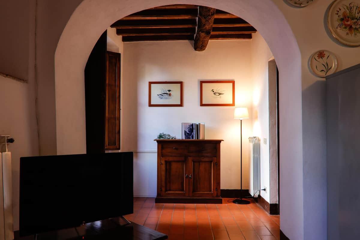 Un interior con televisión, mueble de madera, cuadros enmarcados y una lámpara.