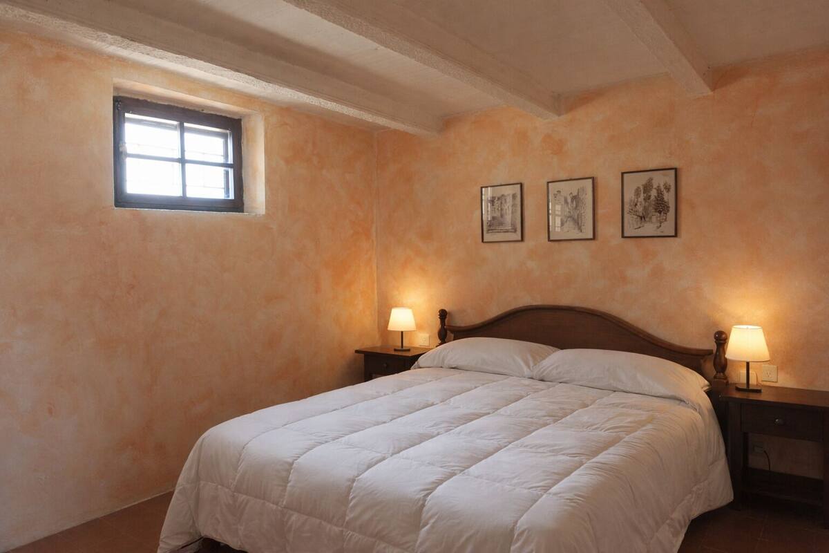Un dormitorio con una cama grande, dos mesitas de noche con lámparas, una ventana y tres cuadros en la pared.