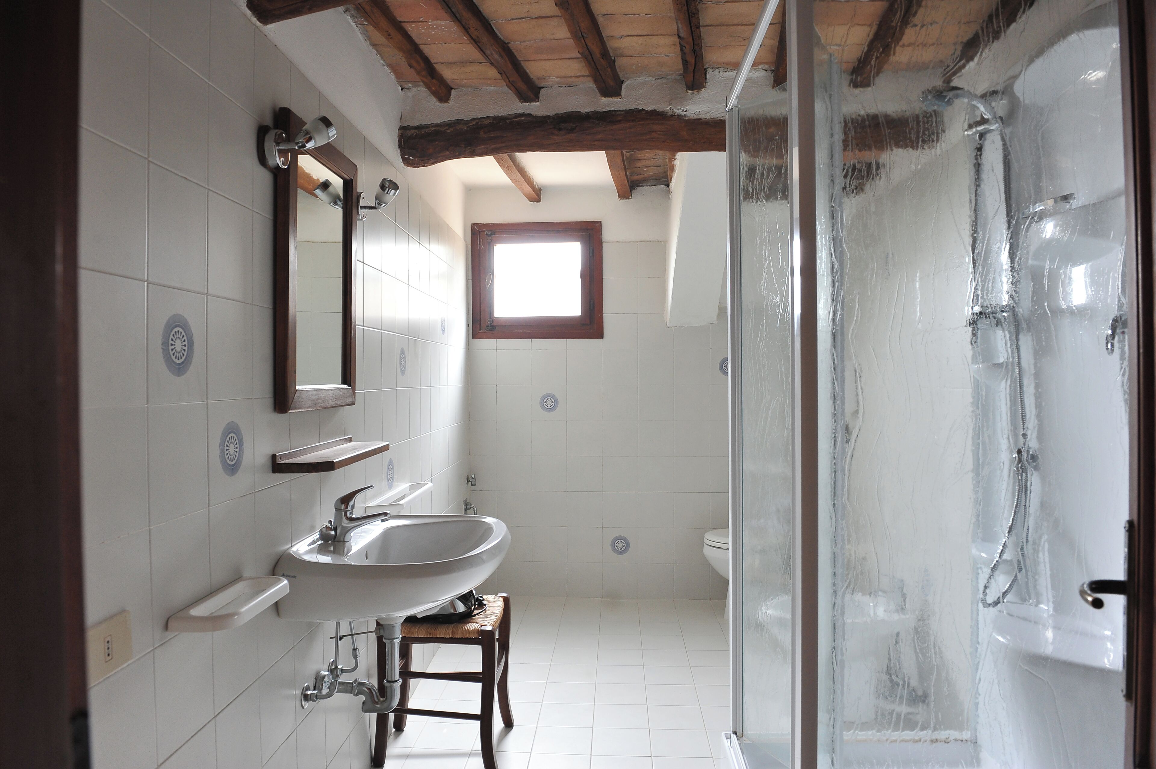 A bathroom with a sink, mirror, shower, and a window.