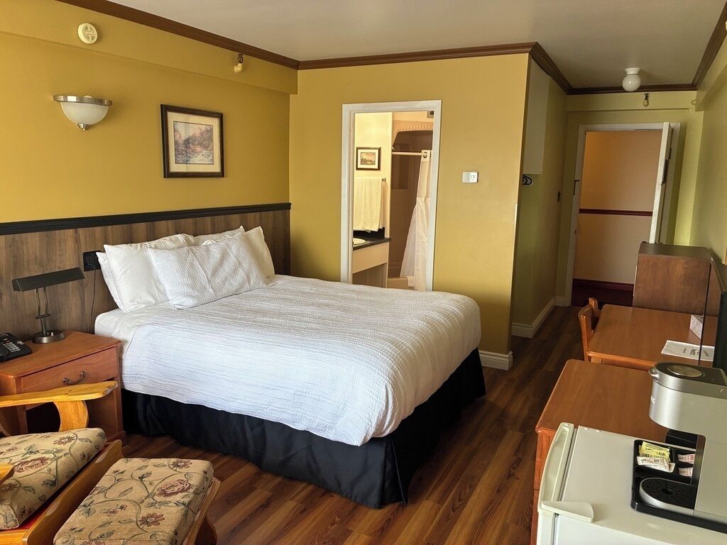 A hotel room with a bed, bedside table, chair, and a desk with a computer.