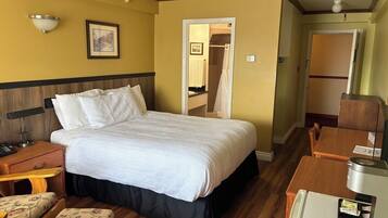 A hotel room with a bed, bedside table, chair, and a desk with a computer.