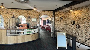 A restaurant interior with exposed brick walls, a wooden counter, and red chairs. - Hotel Motel Le Château (Lac-Megantic)