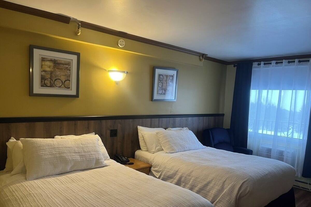 A hotel room with two beds, a nightstand with a phone, and framed artwork on the wall.